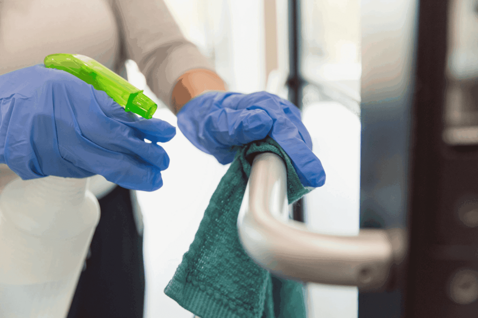 Person cleaning door handle with disinfectant spray.